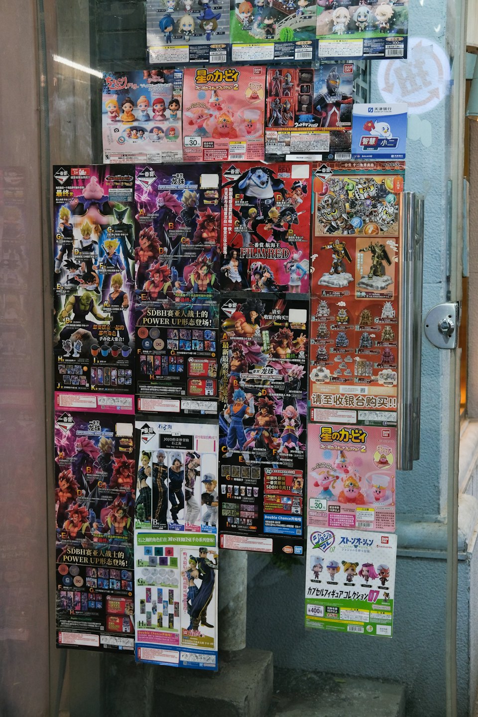 Anime and manga posters fill a cluttered shop window display.